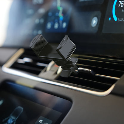 Universalholder til mobil og GPS, sort, monteret på bilens ventilationsgitter med digitalt dashboard svagt synligt i baggrunden.