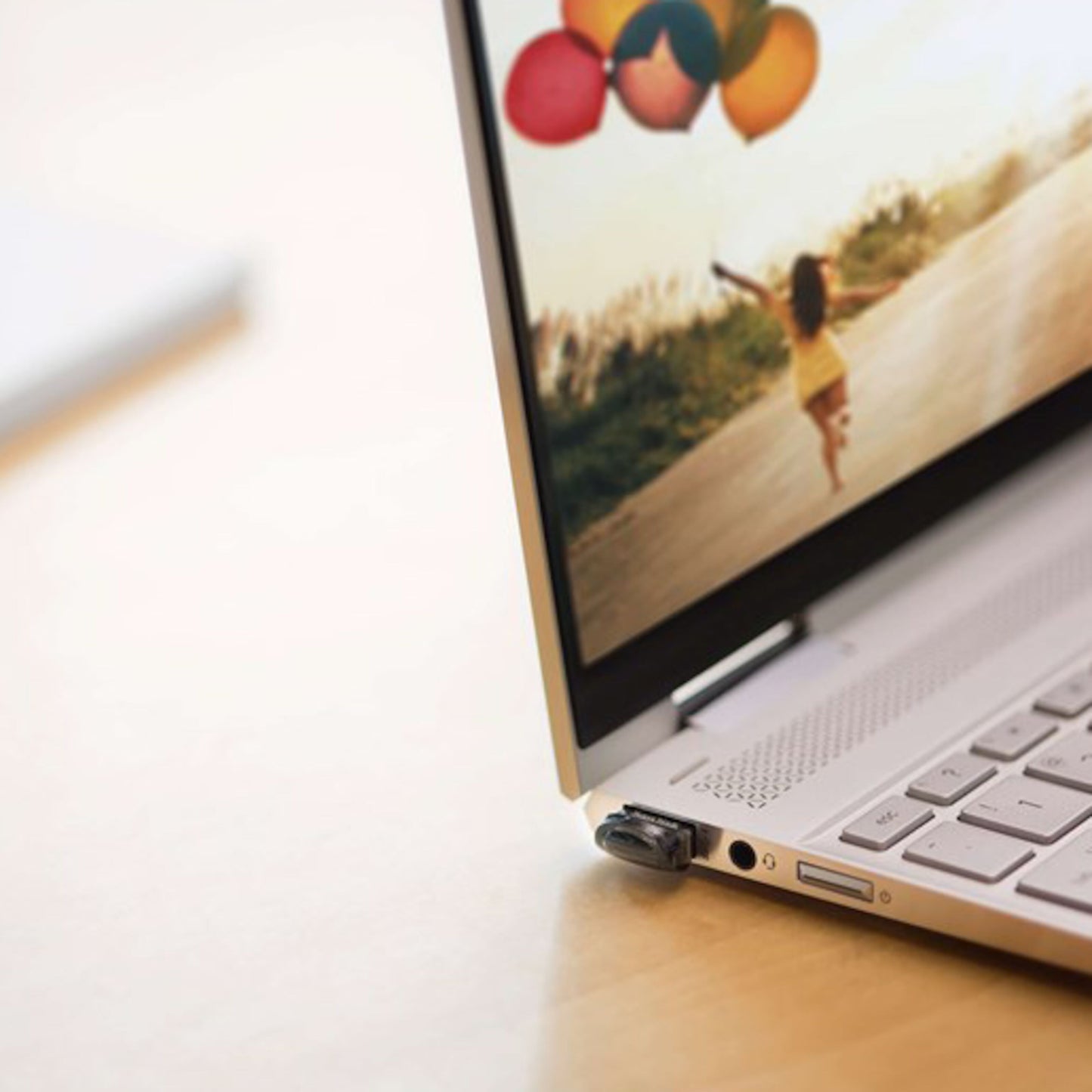 Sandisk Ultra Fit 3.1 USB-nøgle 32 GB tilsluttet laptop, laptopskærm viser barn med farverige balloner.